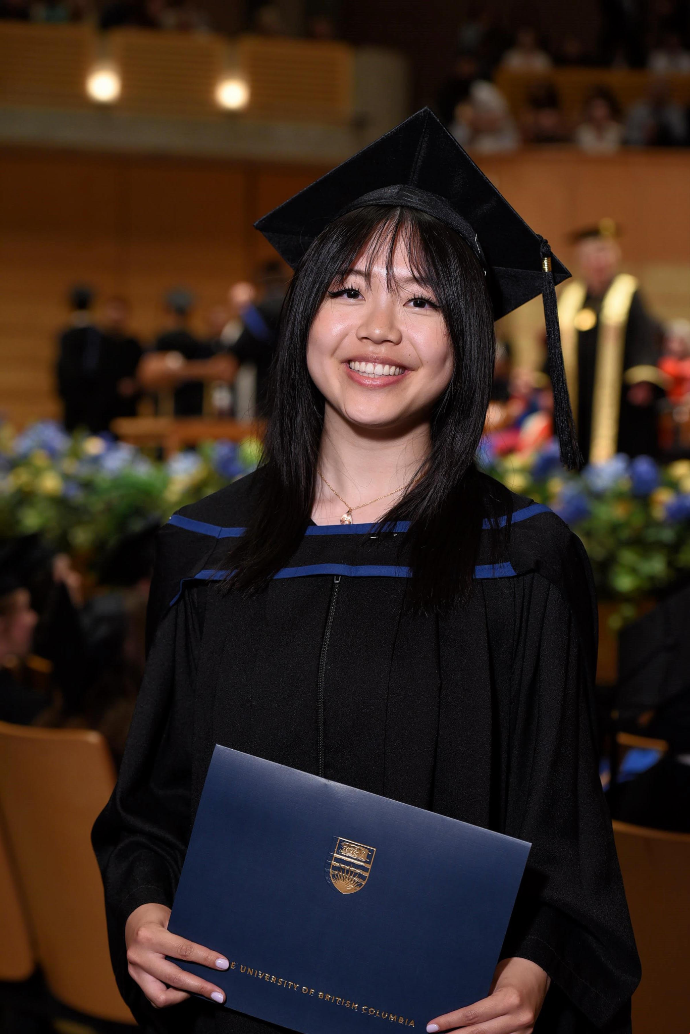 Joyce smiling at her UBC graduation, holding her diploma